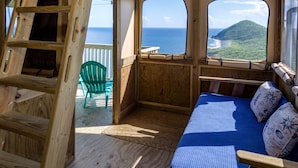 Una cabaña de madera con cama, una silla y vista al océano.