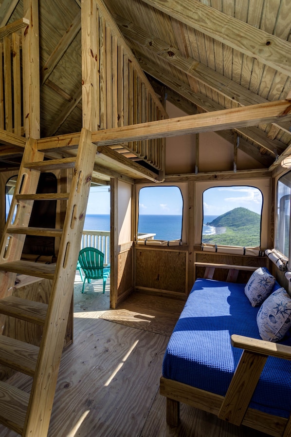 A wooden cabin with a bed, a chair, and a view of the ocean. - Concordia Eco-Resort (St. John)
