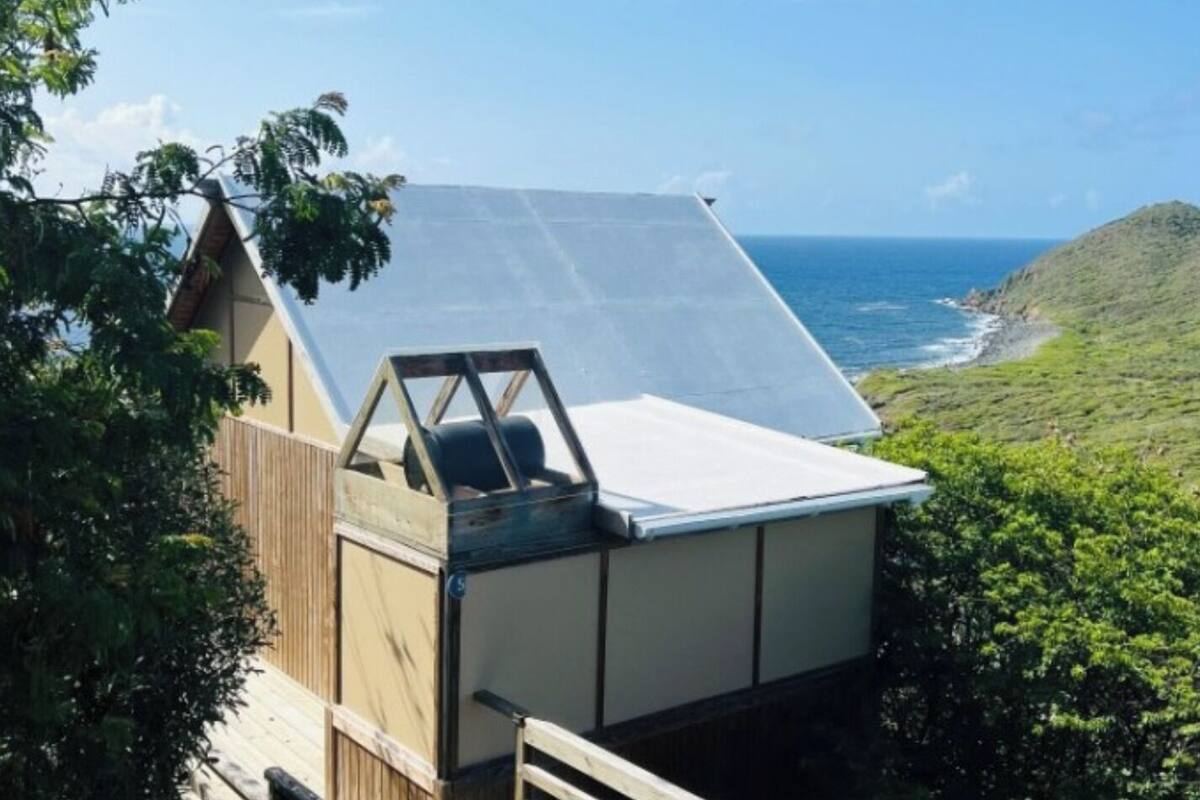 A small, single-story building with a sloped roof, a wooden deck, and a view of the ocean.