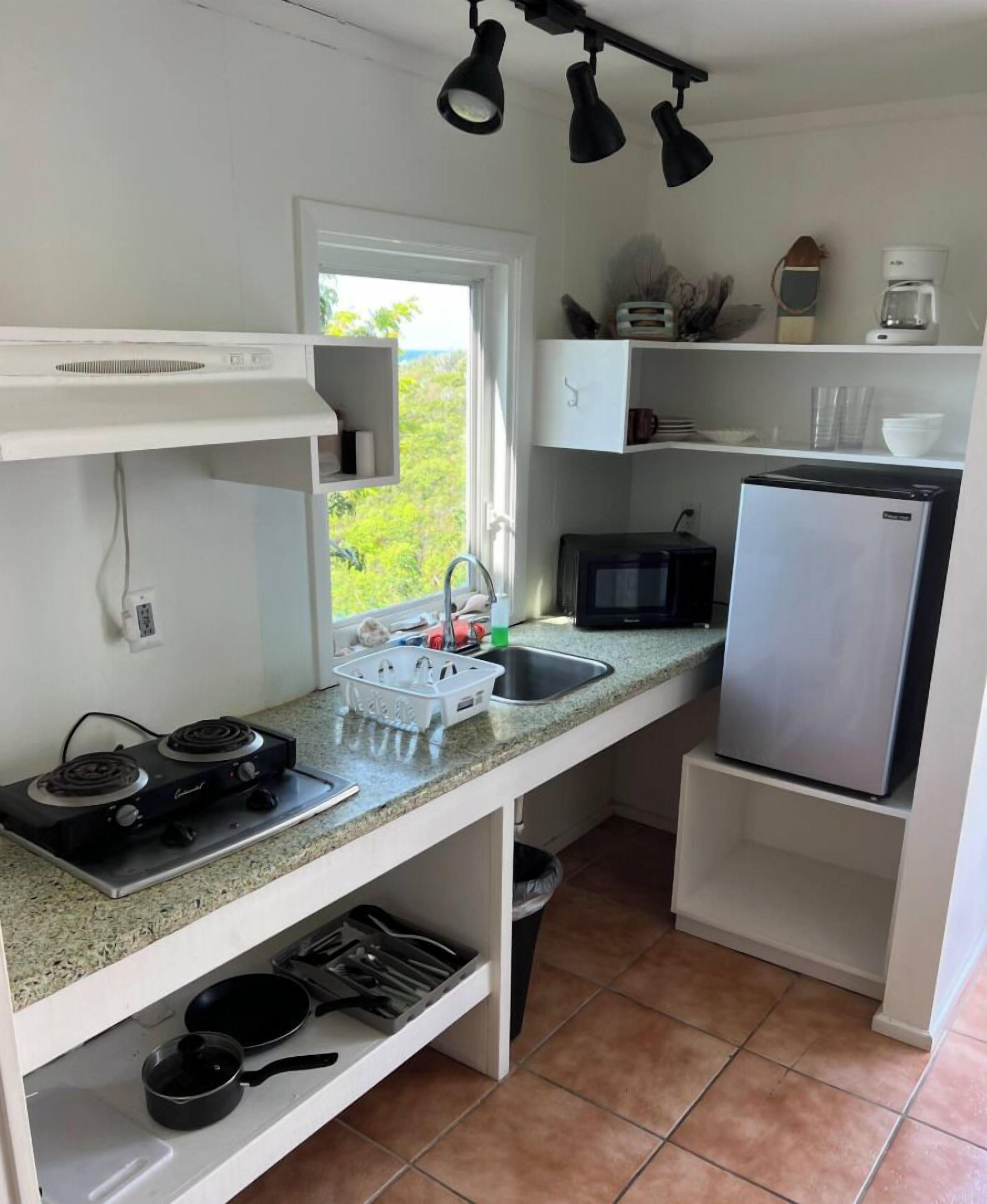 A compact kitchen with a gas stove, a microwave, a refrigerator, and a window providing a view of greenery.