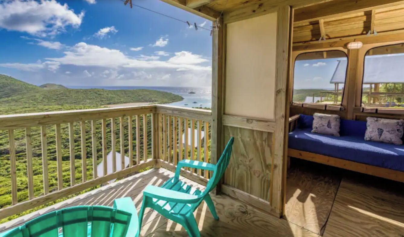A wooden deck with a view of a coastal landscape, a blue sofa, and two turquoise chairs.