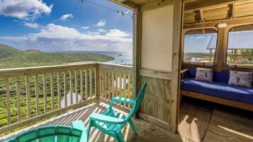 A wooden deck with a view of a coastal landscape, a blue sofa, and two turquoise chairs.