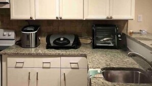 Eine Küche mit weißen Schränken, einer Granit-Arbeitsplatte, einer Kaffeemaschine, einem Toaster und einem Spülbecken.