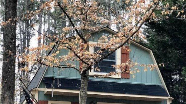 Ein zweistöckiges Haus mit Steinuntergrund, einer Holzdiele und einer roten Tür.