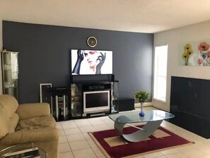 Cozy living space with a flat-screen TV above the fireplace, a glass coffee table, and a comfortable sofa.