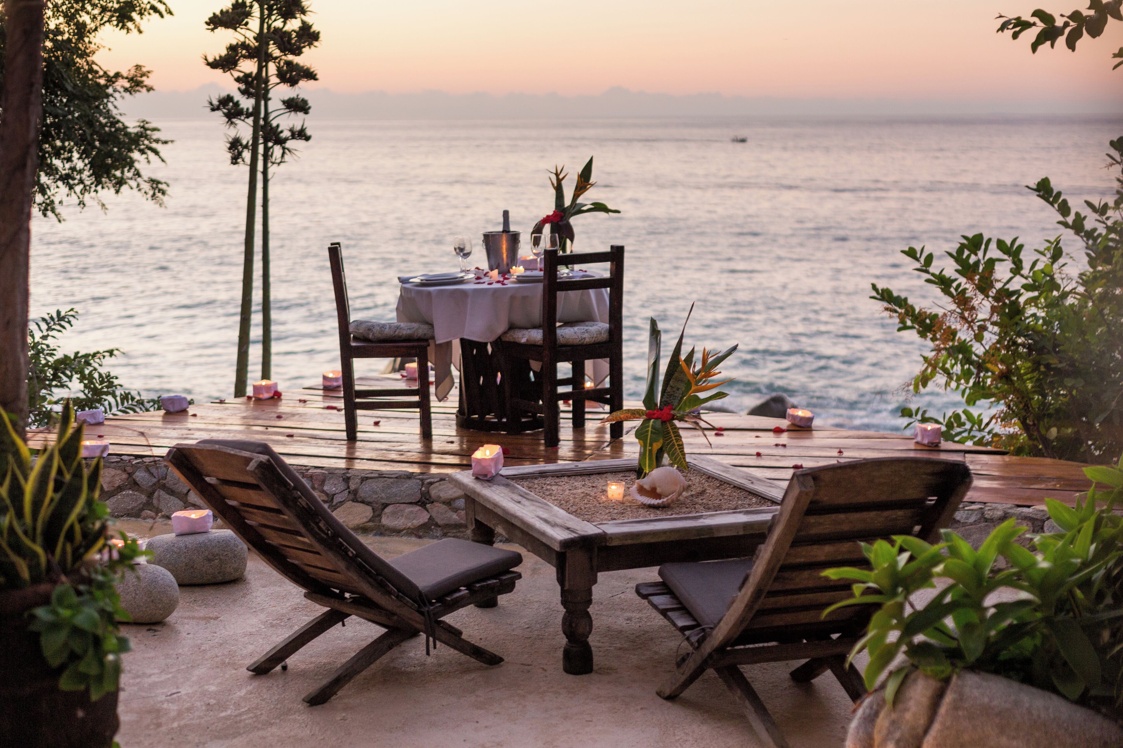 An outdoor dining area with a table and chairs, a view of the sea, and potted plants.