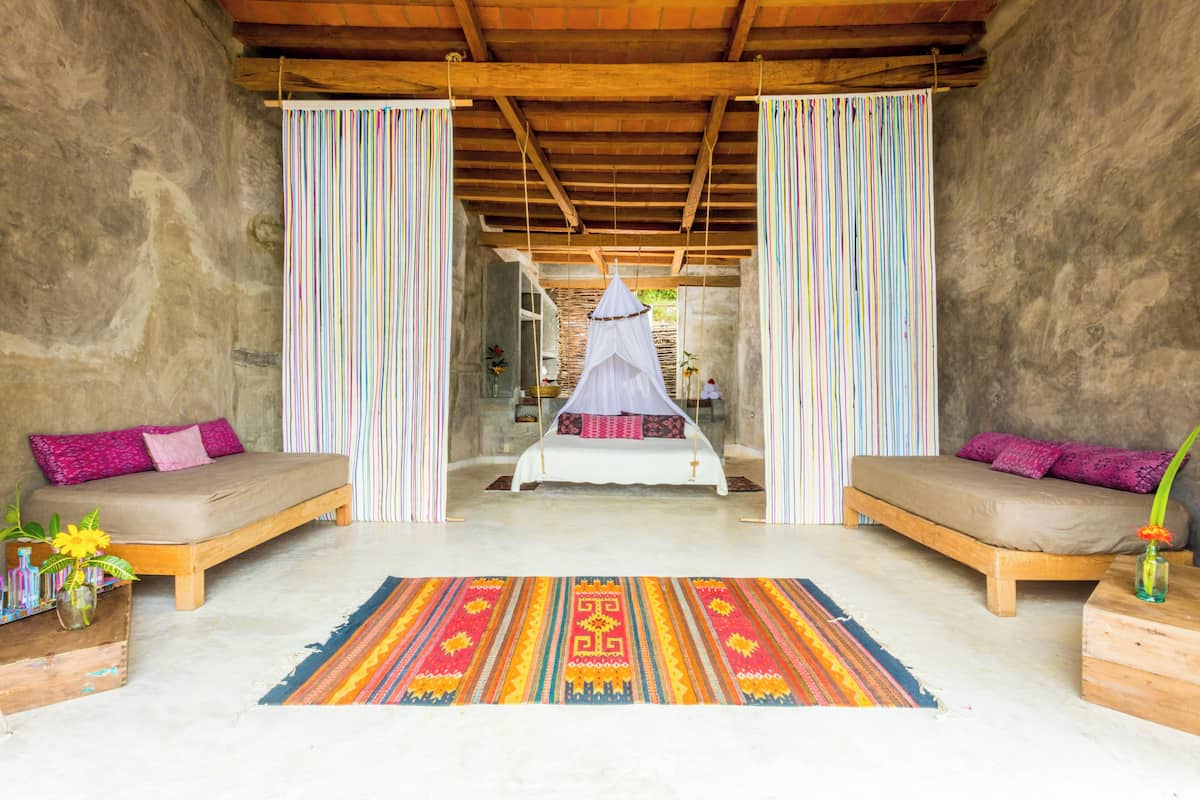 Une pièce comprenant un lit, deux canapés, un tapis coloré et un lit à baldaquin suspendu.