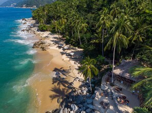 Una playa con palmeras, una cabaña de techo de paja y sillas de descanso.