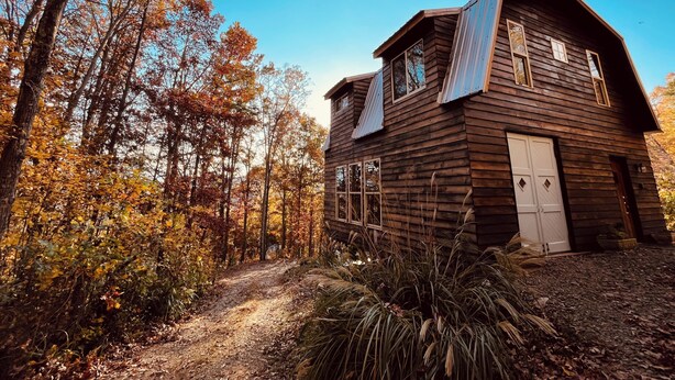 En rustik træhytte med en sti af jord der fører til den, omgivet af efterårsfarver.