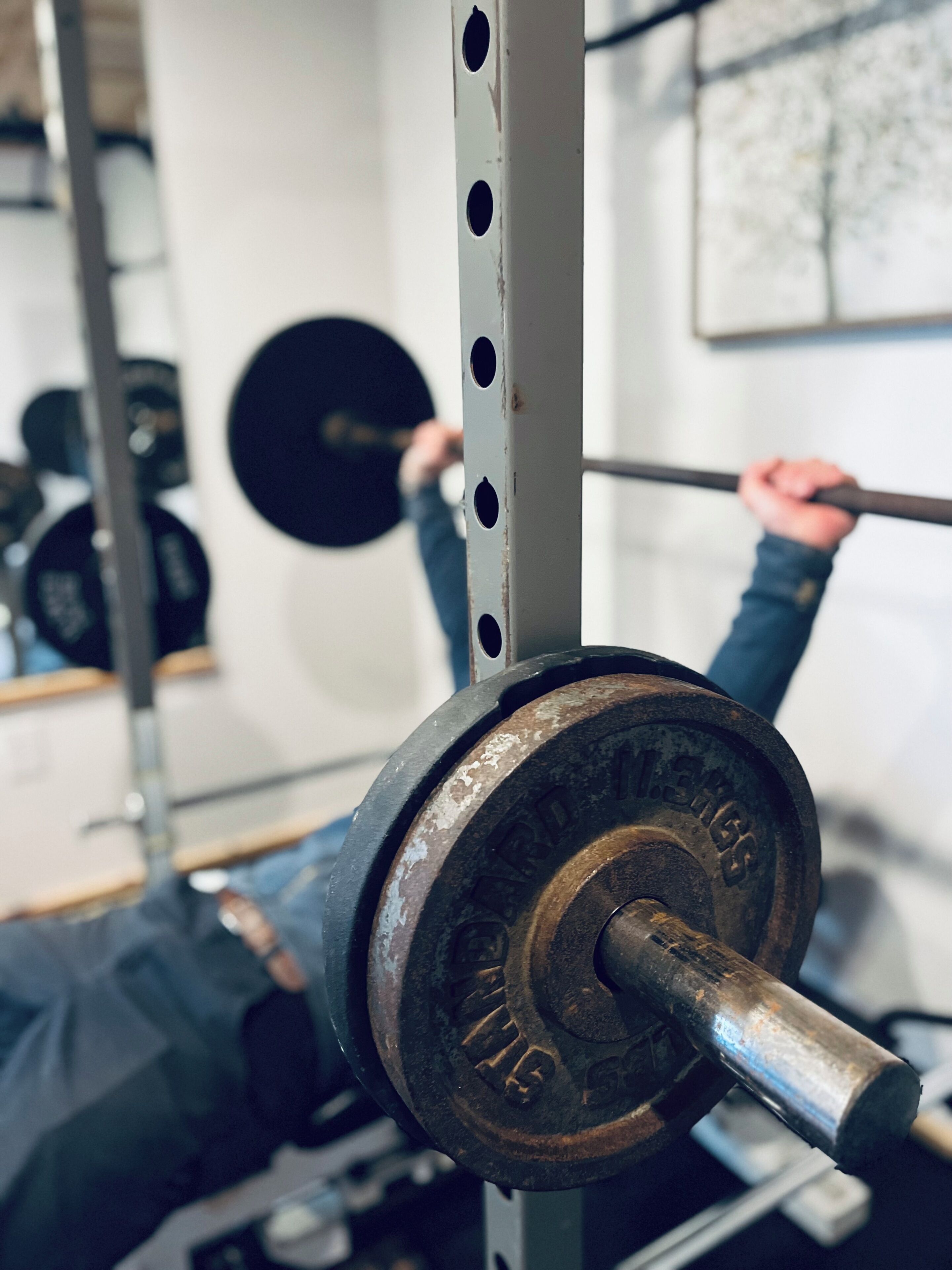 Een halter met gewichtsschijf op een standaard, een metalen frame en een spiegel die iemand bij het gewichtheffen weerspiegelt.