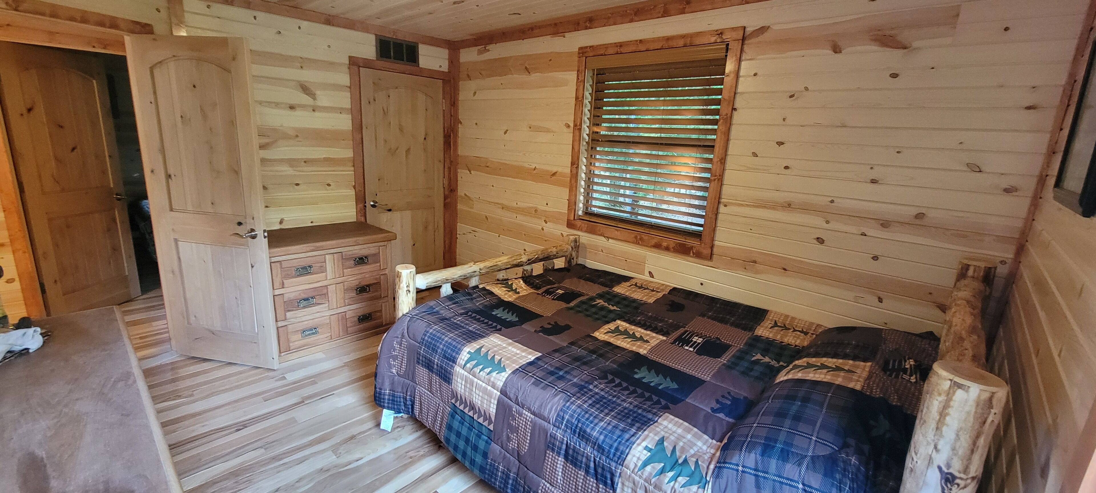 Camera da letto in una baita di legno, con un letto, una cassettiera e una finestra con persiane.
