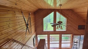 Una cabaña de madera con techos altos, un tragaluz grande y un ventilador de techo.