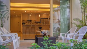 A modern living room with a glass door leading to a kitchen, white plastic chairs, and a small table with two wine glasses. - San Diego 974 Suites (Cartagena)