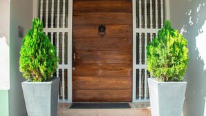 A wooden door with a metal knocker, flanked by two potted plants and white decorative panels. - San Diego 974 Suites (Cartagena)