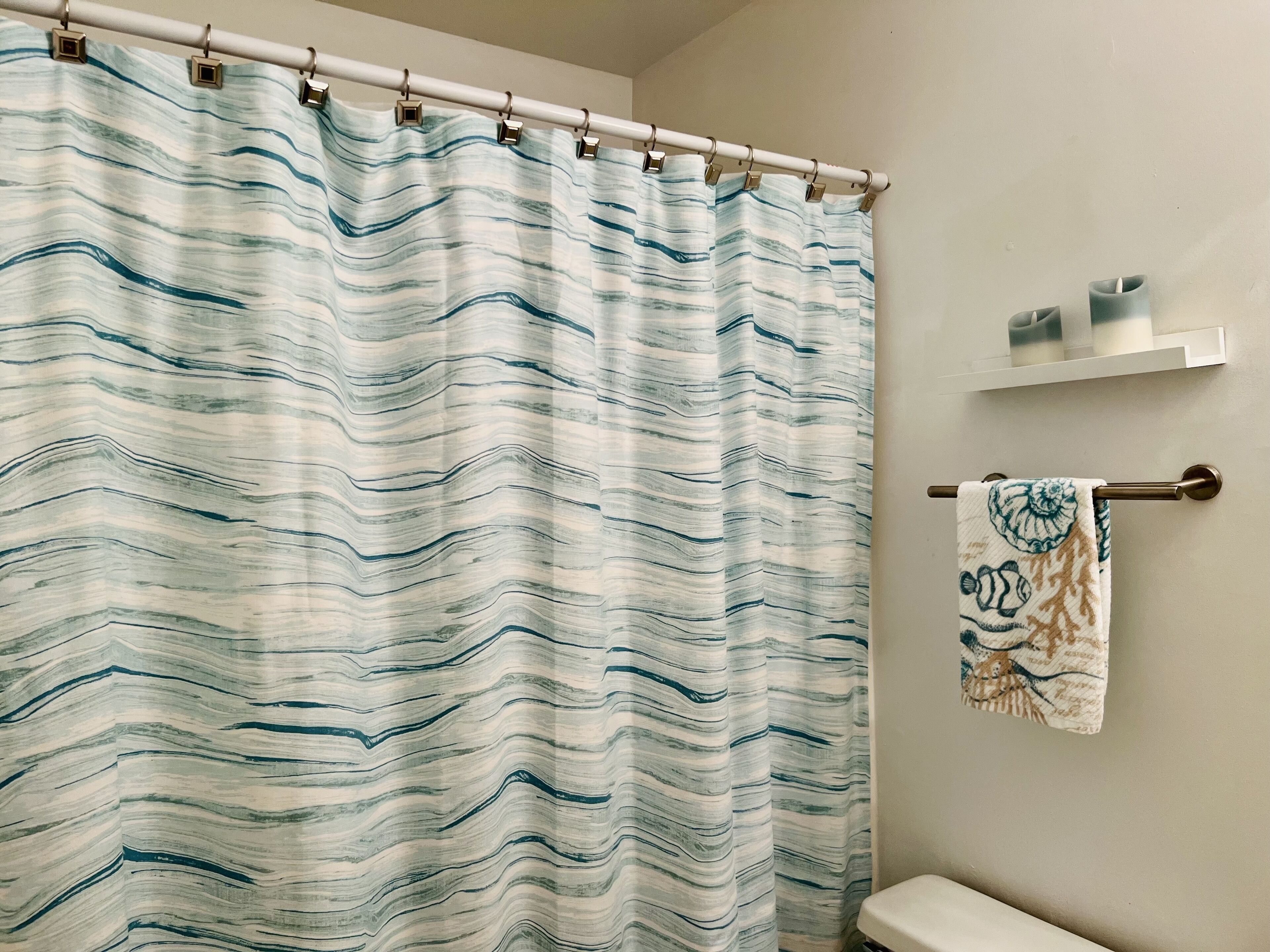 Une salle de bain avec un rideau de douche à rayures, un porte-serviettes orné d’une serviette décorative et une étagère contenant des articles de toilette.