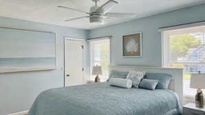 Una camera da letto con un letto, una ventola a soffitto, una finestra con persiane e un'opera d'arte incorniciata appesa al muro.