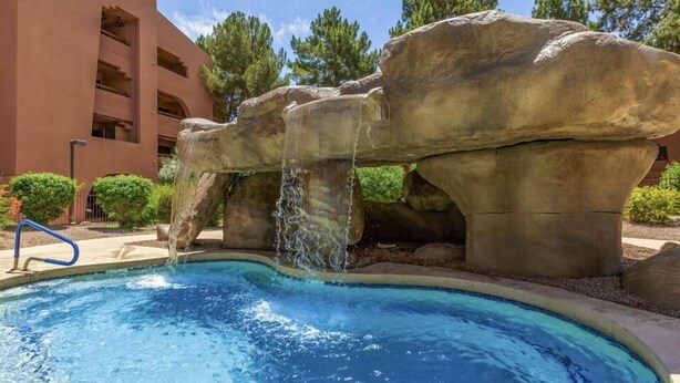 Una piscina con cascada, rodeada de rocas grandes y vegetación.