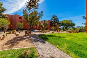 A courtyard with a paved walkway, cacti, and trees, surrounded by buildings with a reddish-brown facade. - CASA EVA - Anasazi Village - Steps from a heated pool (Phoenix, Arizona)