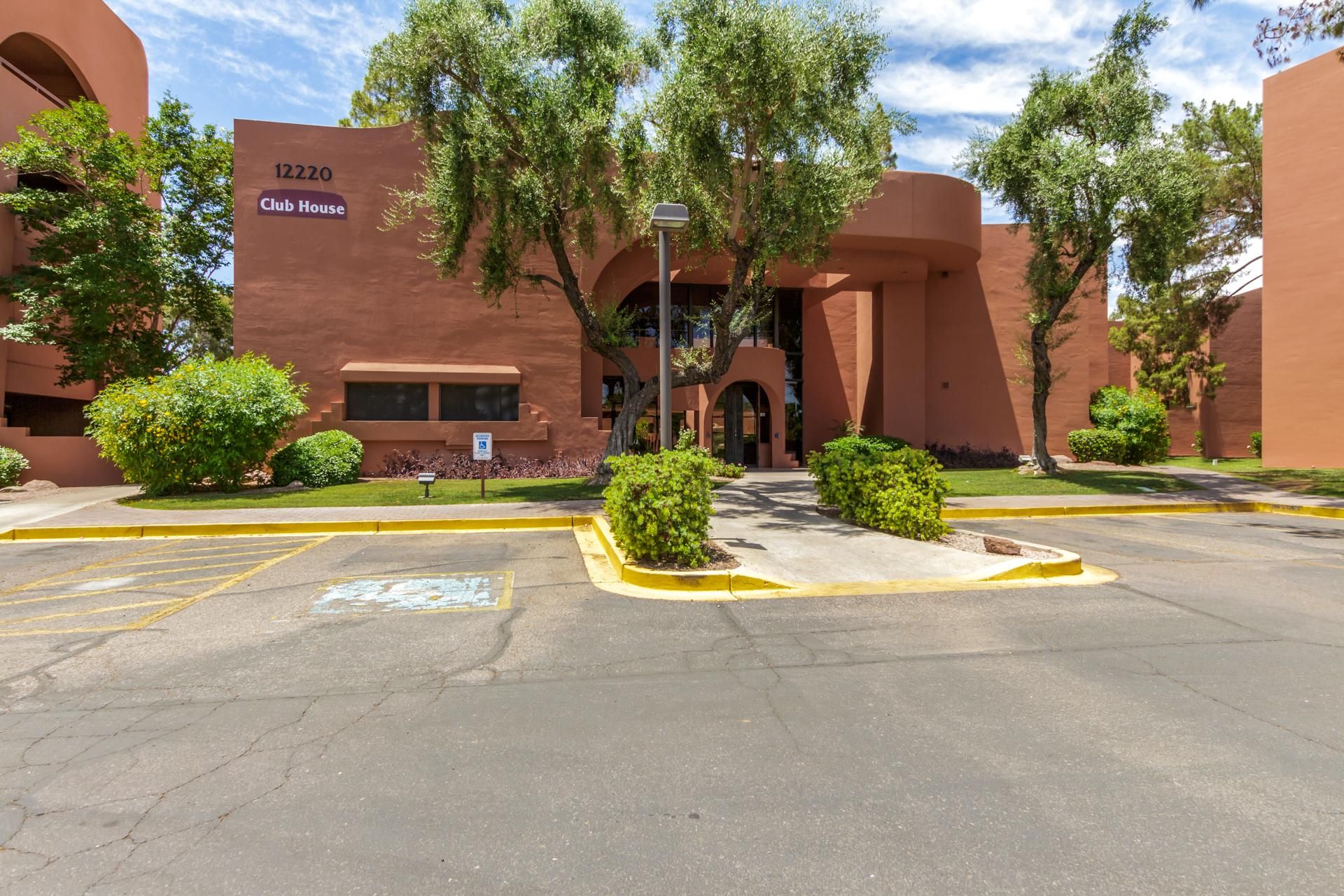 A building with a sign reading "12220 Club House" and a parking lot with yellow curbs and marked spaces.