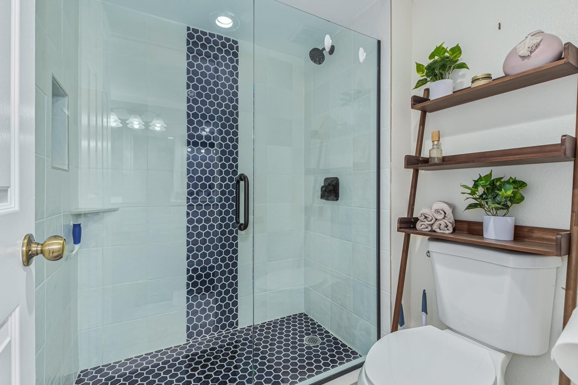 A modern bathroom with a glass shower enclosure, a toilet, and wooden shelves with toiletries.