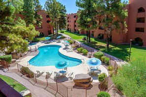 A swimming pool with lounge chairs and umbrellas, surrounded by a fence and trees. - CASA PACIFICO - Anasazi Village - Plush 2 bed/1 bath unit (Phoenix)