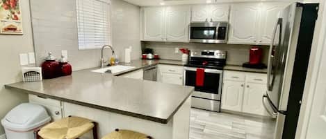 A modern kitchen with white cabinetry, a central island with stools, stainless steel appliances, and a ceiling fan.