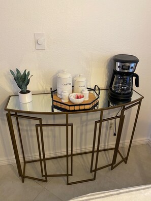 A glass-top coffee station with a coffee maker, sugar and coffee containers, and a small plant. - CASA AVENTURA - Anasazi Village - Pool View (Phoenix)