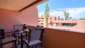 Un balcone con tavolo e sedie, con vista su un edificio con diversi balconi e alberi.