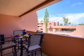 Ein Balkon mit Tisch und Stühlen, mit Blick auf ein Gebäude mit mehreren Balkonen und Bäumen.