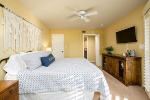 A bedroom with a bed, a ceiling fan, a TV, a wooden dresser, and a macrame wall hanging. - CASA MONTANA - Anasazi Village - 2nd Floor View (Phoenix)