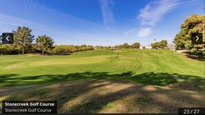 Un campo de golf con cielo despejado, césped cuidado y árboles.