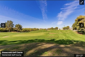 A golf course with a clear sky, well-maintained grass, and trees.