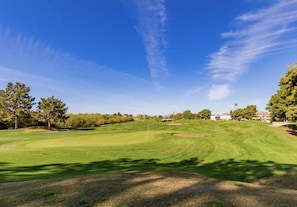 Um campo de golfe com céu claro, grama bem cuidada e árvores.