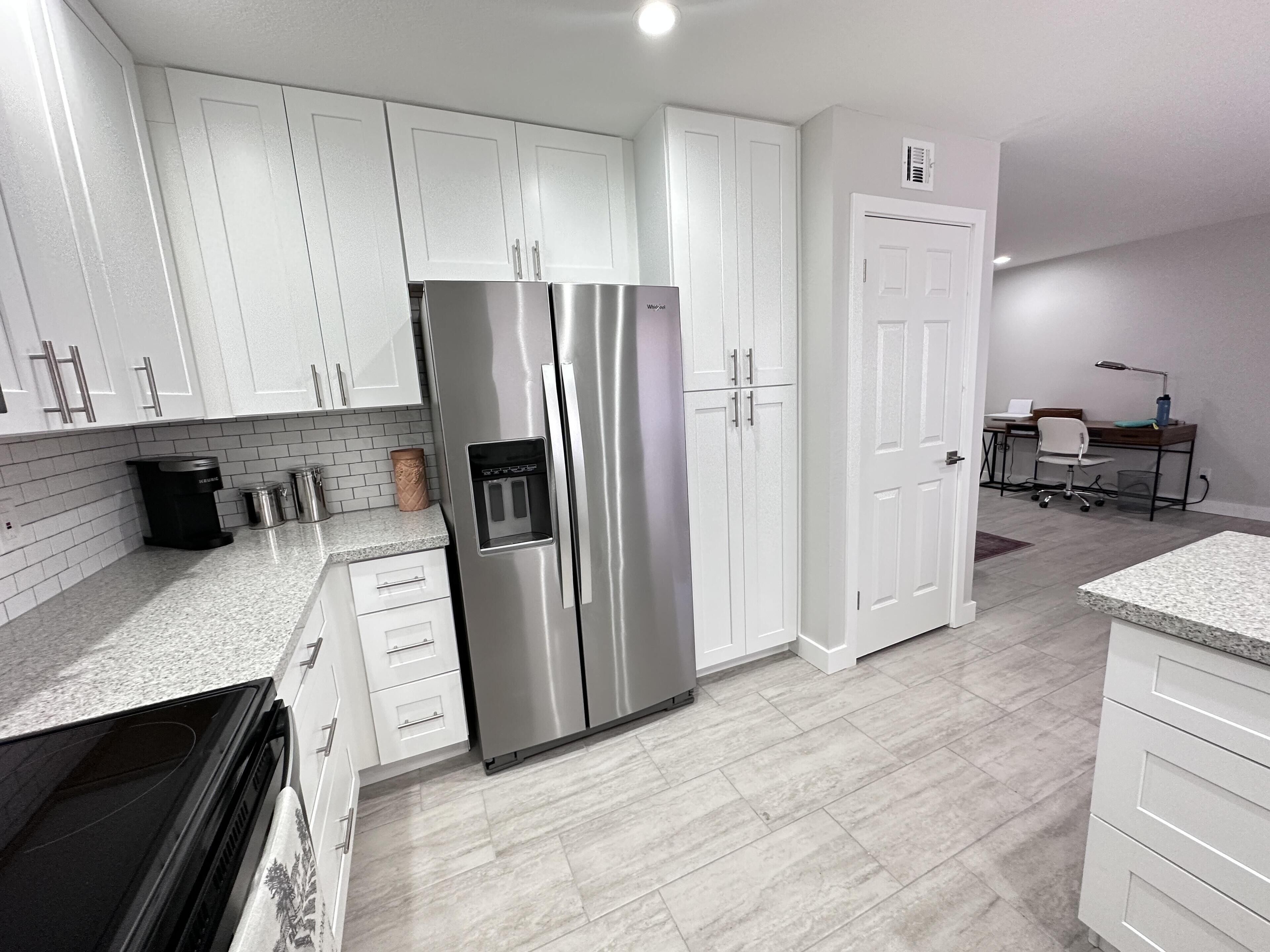 A modern kitchen with white cabinets, a stainless steel refrigerator, granite countertops, and a tiled backsplash.