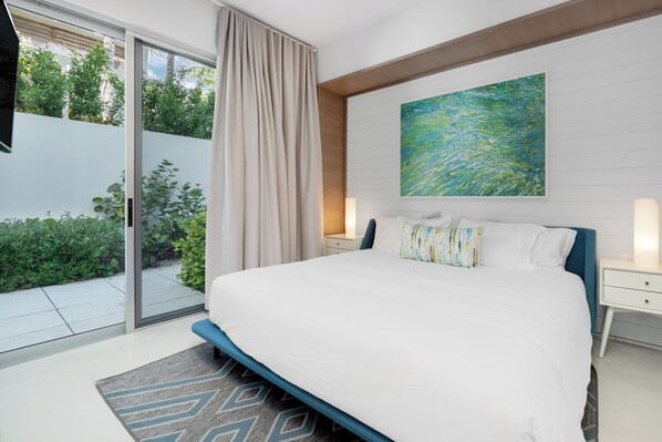 Une chambre moderne avec un grand lit, une porte-fenêtre coulissante donnant sur un balcon et un tableau accroché au mur.
