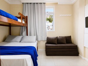 Quarto com beliche, sofá, janela com cortinas e televisão na parede.