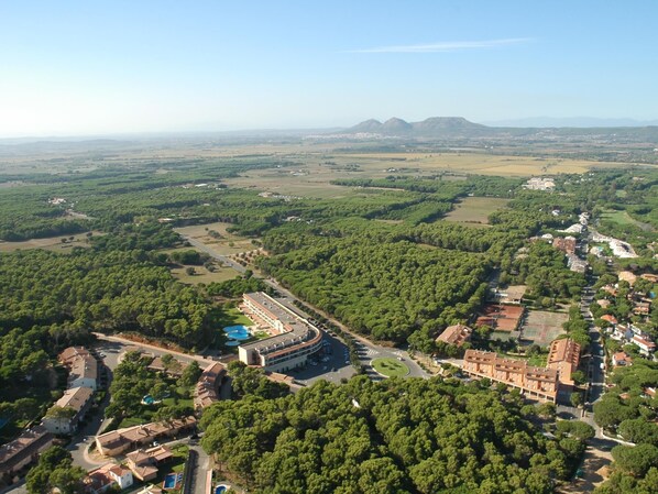 An aerial view of a resort with a large building, swimming pools, and surrounding greenery.
