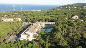 Vista aérea de um hotel com um amplo estacionamento, piscina e vista para o mar.