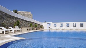 A swimming pool with lounge chairs and a stone wall. - Belogna Ikons (Naxos)