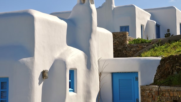 A white building with blue doors and windows, stone walls, and a stone staircase. - Belogna Ikons (Naxos)