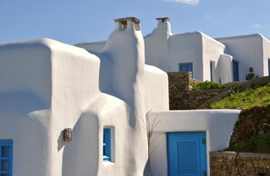 A white building with blue doors and windows, stone walls, and a stone staircase. - Belogna Ikons (Naxos)