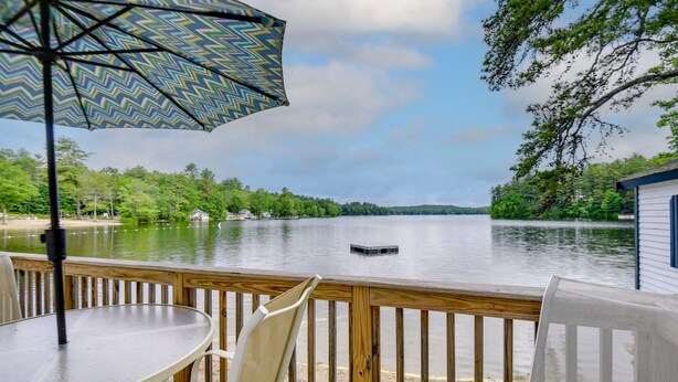 Une terrasse en bois avec une table et des chaises, donnant sur un lac paisible où se trouve un quai.