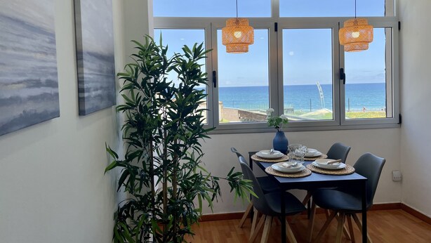 A dining area with a table set for four, large windows with a view of the ocean, a potted plant, and two hanging lights. - Las Canteras View Home (Las Palmas de Gran Canaria)