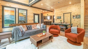 A spacious living area with a sofa, chairs, and a coffee table. There is a kitchen in the background with cabinets and a dining table.