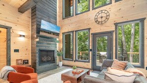 A modern log cabin interior with a fireplace, large windows, and a cozy seating area.
