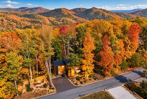 A cabin surrounded by autumn foliage with a paved driveway and a clear view of the surrounding hills.