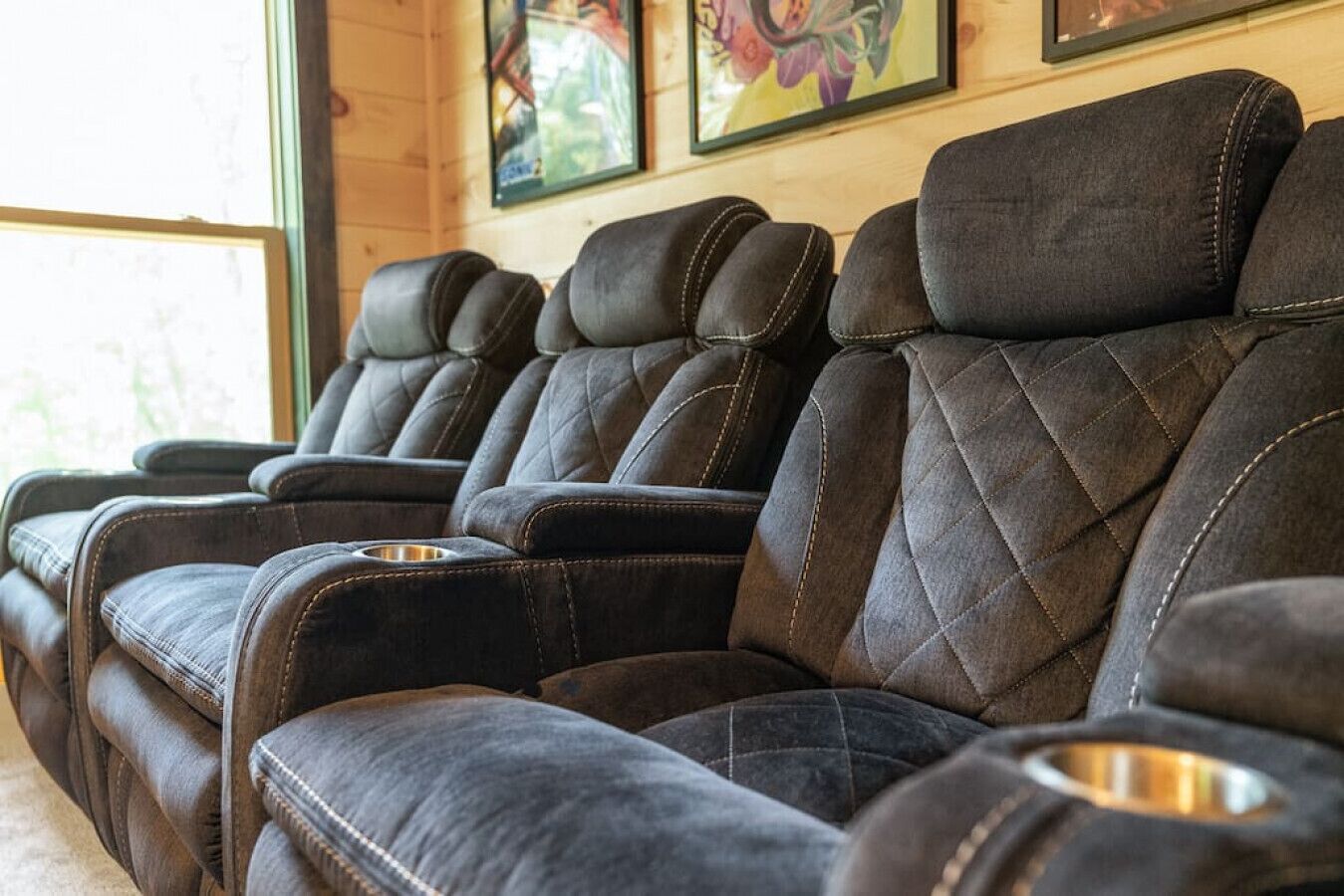 A row of dark leather massage chairs with armrests and footrests, arranged in a row against a wooden wall with framed artwork above.