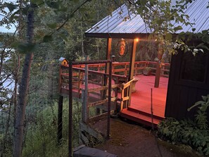 Une terrasse en bois avec un plancher rouge, entourée d’arbres et surmontée d’une structure de toit en métal.
