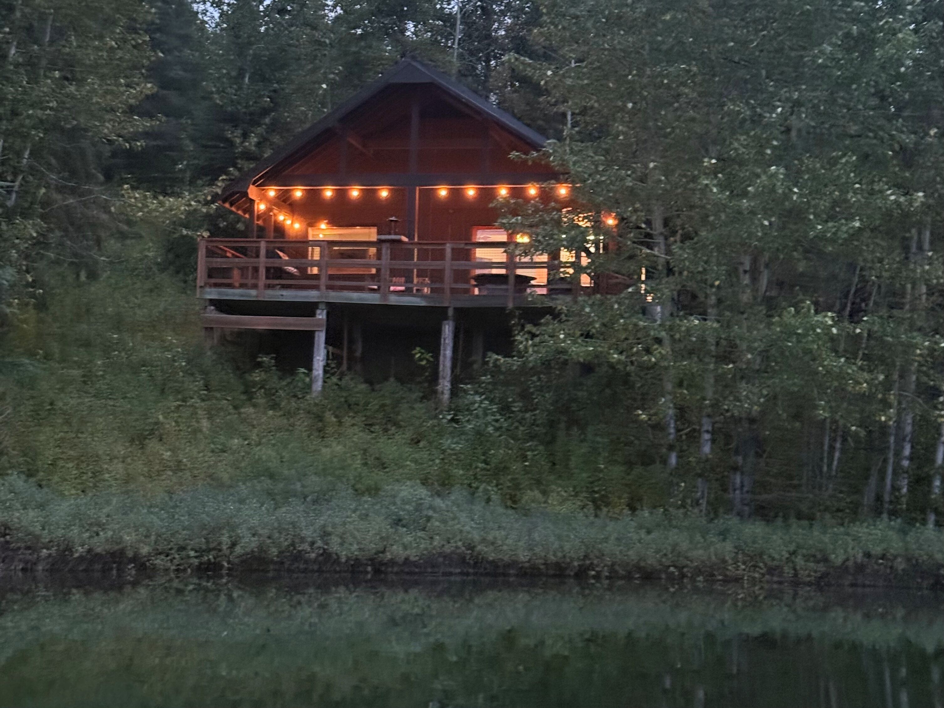 Una cabaña de madera con balcón, rodeada de árboles y una masa de agua.