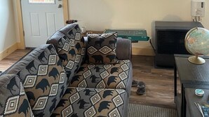 A living room with a sofa, a flat-screen TV mounted on the wall, a small table with a globe, and a heater. - Alaska Summers Lodge Loft-Near Mouth of Kasilof River (Cohoe)